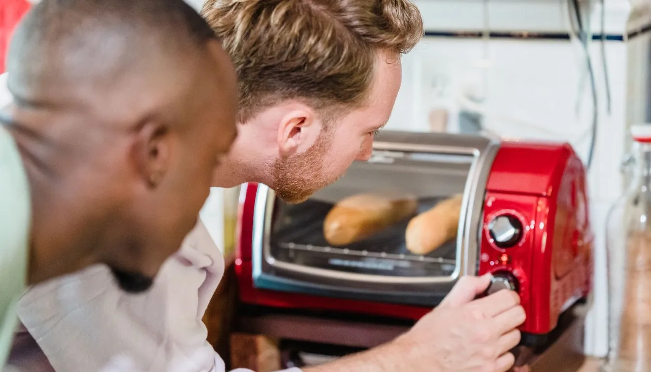 Two men checking bread toasting in a red toaster oven