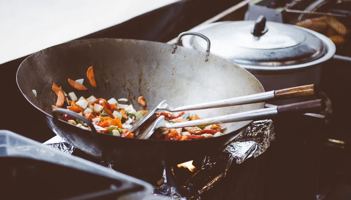 Vegetables stir-frying in a carbon steel wok over flame