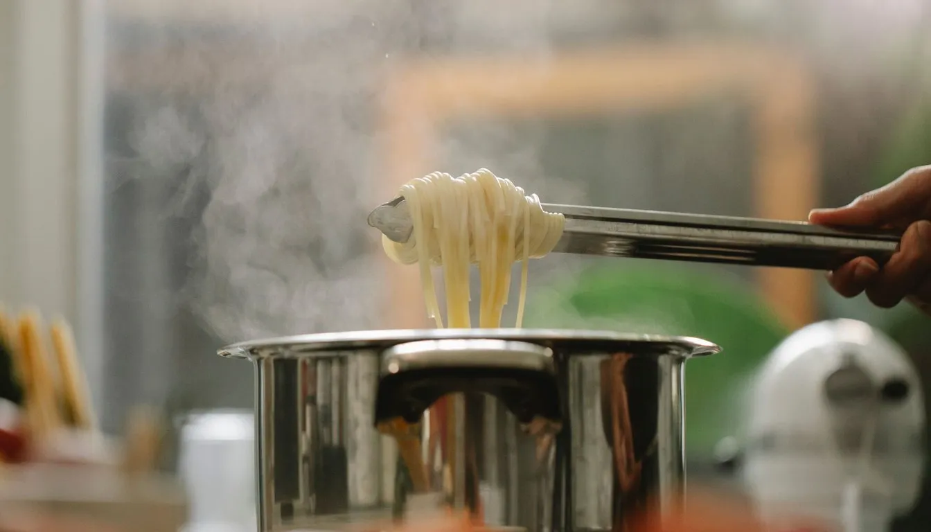Tongs lifting pasta from a steaming stainless steel pot