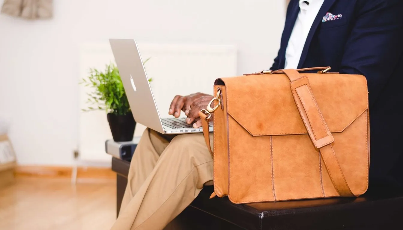 Tan leather briefcase beside a man working on a laptop