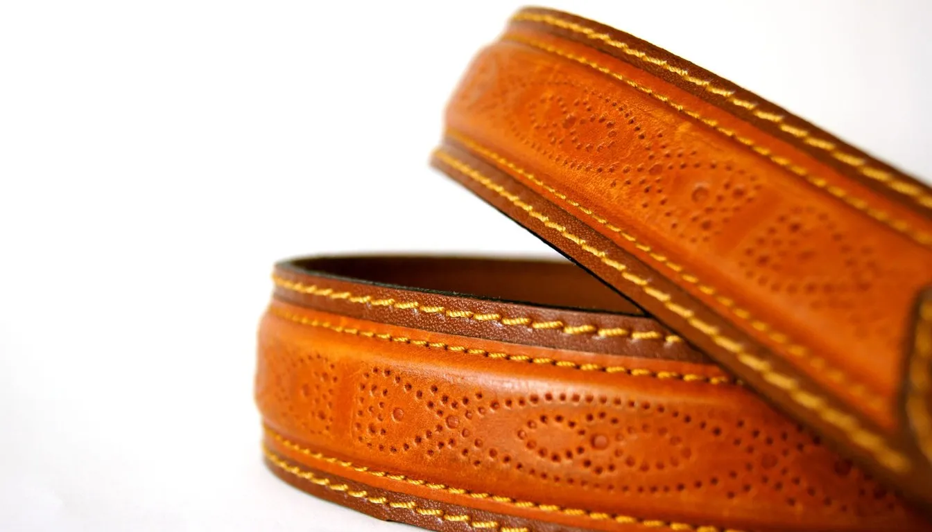 Tooled tan leather belts coiled on a white background
